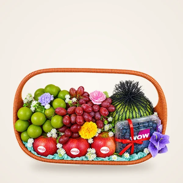 Grand Elegance Festive Fruit Basket - apples, red and green grapes, blueberries, pomelo and flowers in a woven handle basket